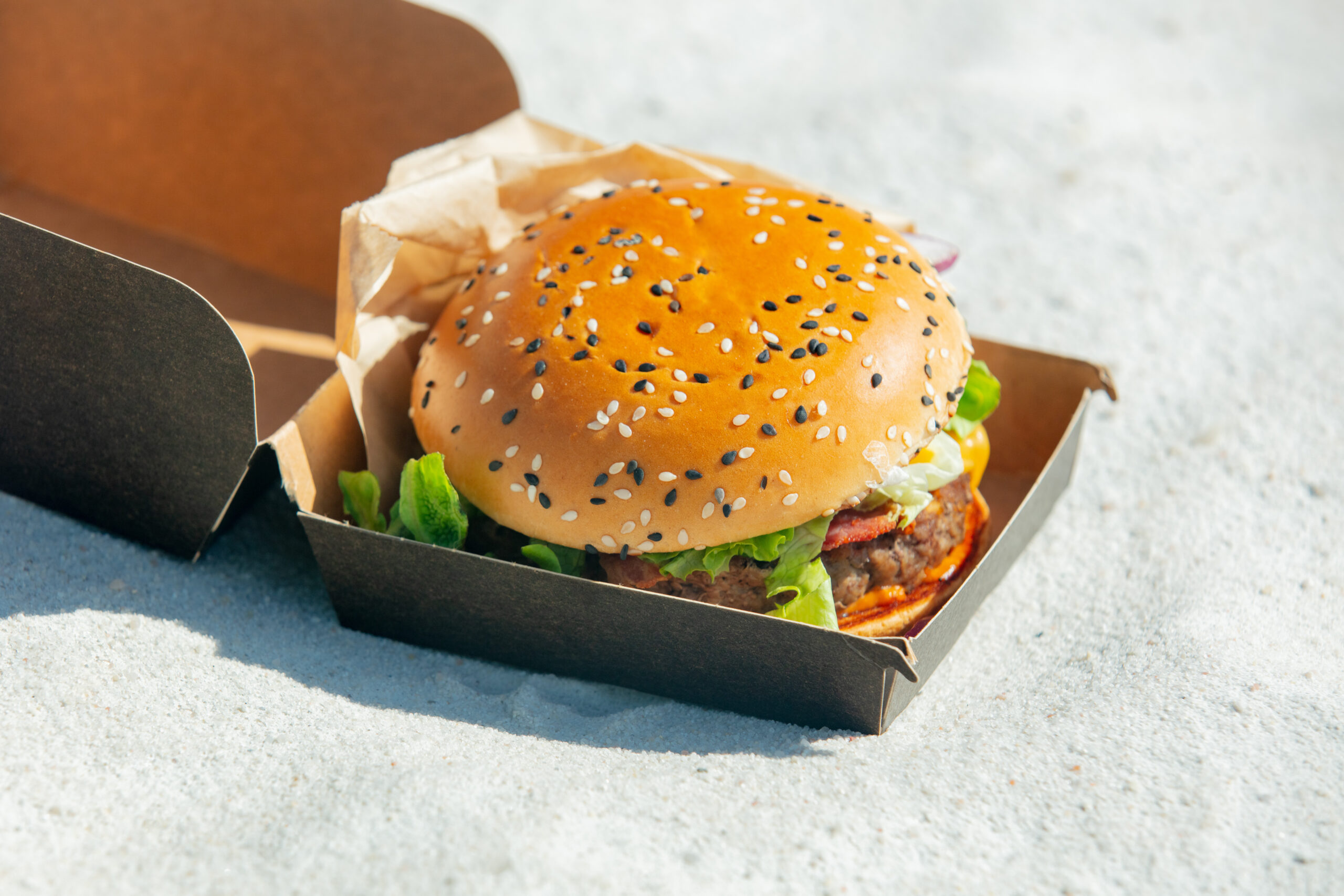 tasty burger in box on white sand on beach 2026 01 05 04 32 17 utc