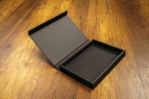 Black custom apparel box open on a wooden surface for premium clothing packaging.